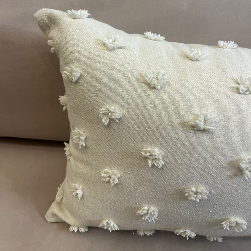 Ivory rectangular throw pillow with textured pom pom details placed on a beige sofa