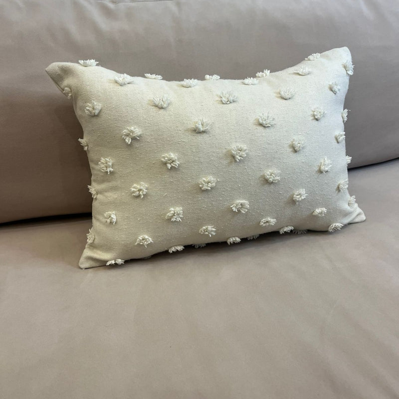 Ivory rectangular throw pillow with textured pom pom details placed on a beige sofa
