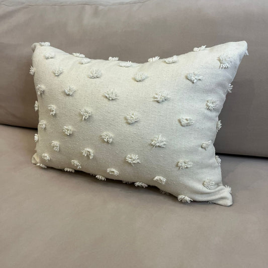 Ivory rectangular throw pillow with textured pom pom details placed on a beige sofa