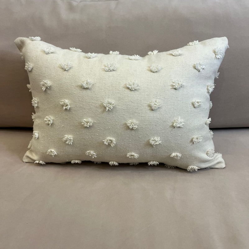 Ivory rectangular throw pillow with textured pom pom details placed on a beige sofa