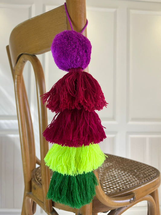 Handmade color block pom pom tassel hanging decor with purple, burgundy, neon green, and green yarn tassels on wooden chair