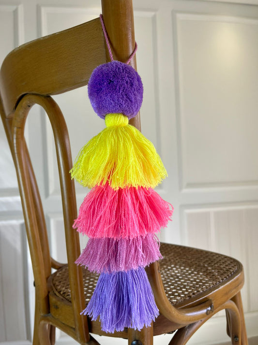 Handmade rainbow pom pom tassel hanging decor with colorful layered yarn tassels displayed on wooden chair