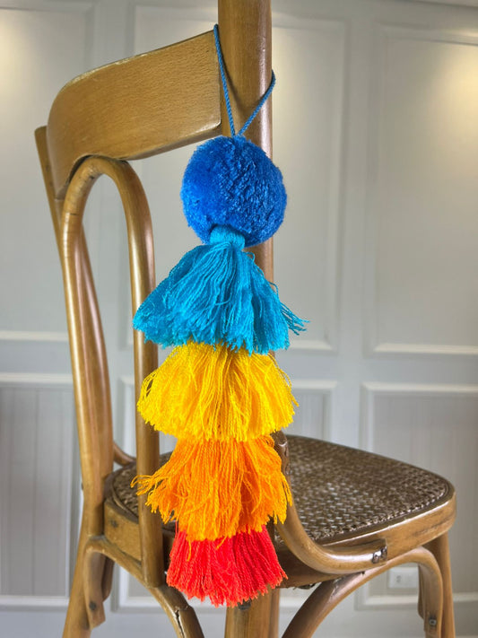 Handmade rainbow gradient pom pom tassel hanging decor with layered colorful yarn tassels displayed on wooden chair