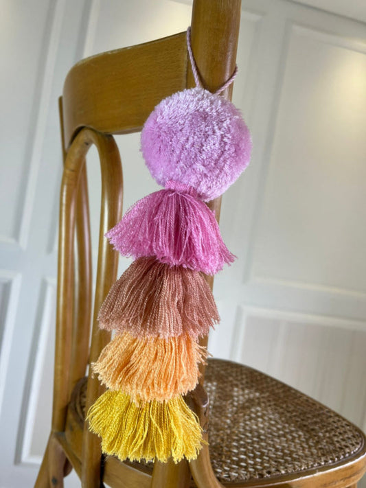 Handmade blush pink pom pom tassel hanging decor with layered warm-toned yarn tassels displayed on wooden chair