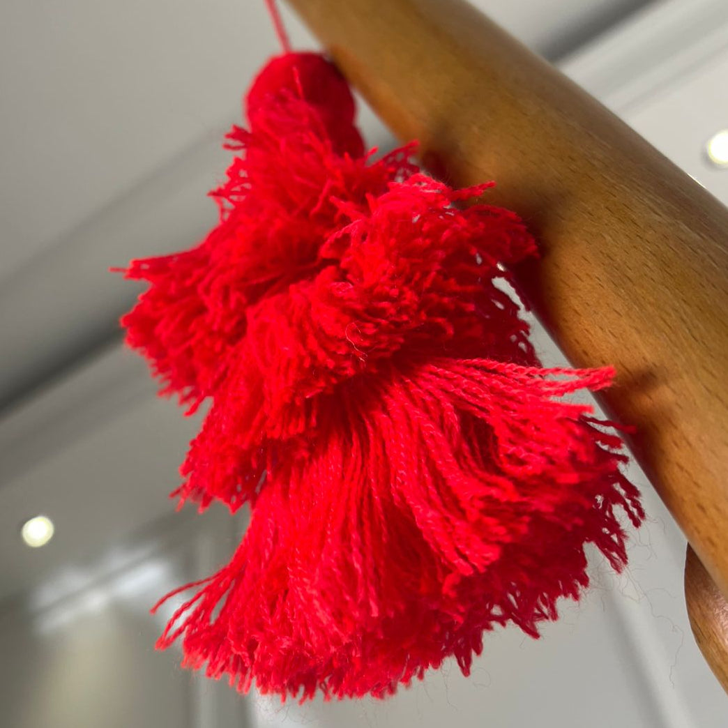 Classic red pom-pom tassel hanging decoration with two pom-poms and layered red yarn tassels hanging on a wooden chair.