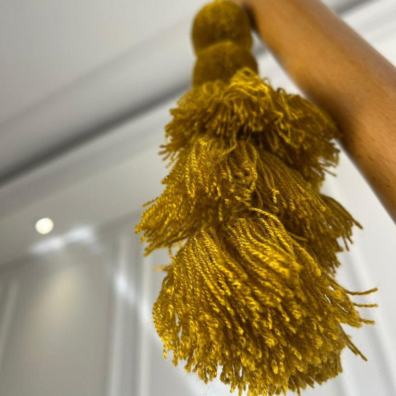 Mustard gold pom-pom tassel hanging decoration with layered yarn tassels hanging on a wooden chair.