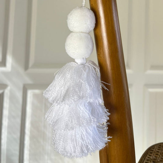 Minimalist white pom-pom tassel hanging decoration with layered white yarn tassels hanging on a wooden chair.