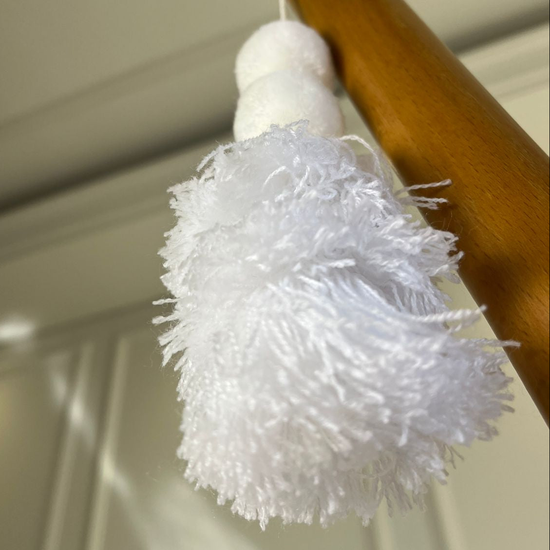Minimalist white pom-pom tassel hanging decoration with layered white yarn tassels hanging on a wooden chair.