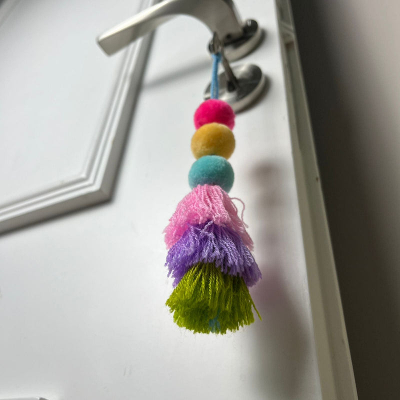 Handmade colorful pom pom tassel hanging decor with layered yarn tassels and bright pom poms on white door background