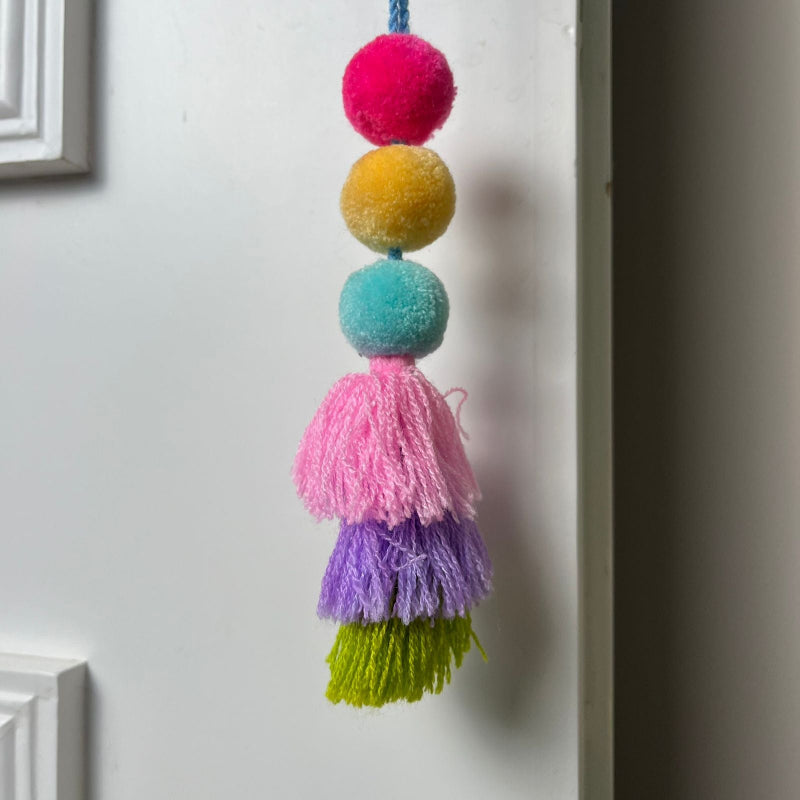 Handmade colorful pom pom tassel hanging decor with layered yarn tassels and bright pom poms on white door background
