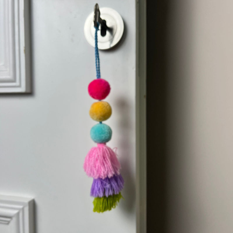 Handmade colorful pom pom tassel hanging decor with layered yarn tassels and bright pom poms on white door background