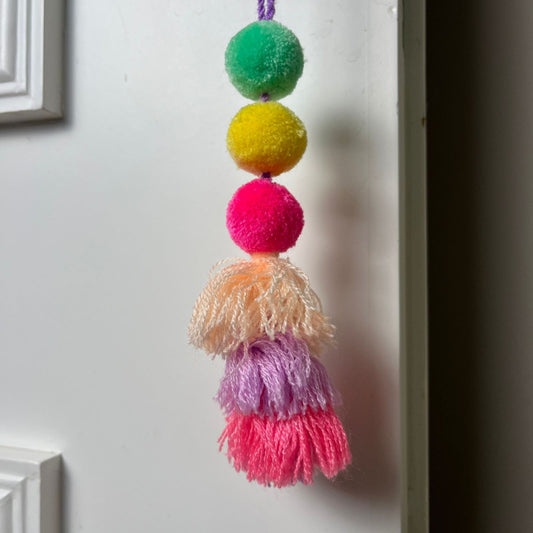 Handmade multicolor pom pom tassel hanging decor with layered yarn tassels on white door background