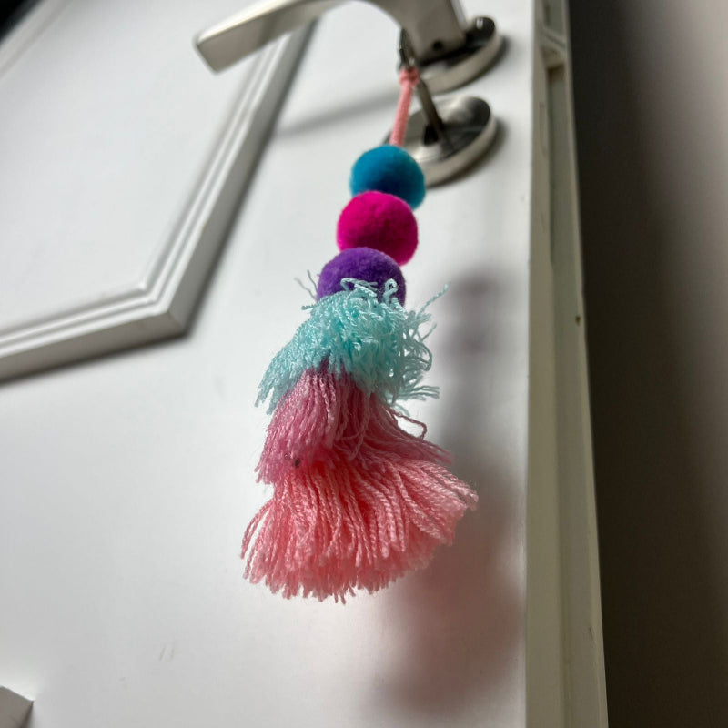Handmade pom pom tassel hanging decor with colorful pom poms and layered pastel yarn tassels on white door background