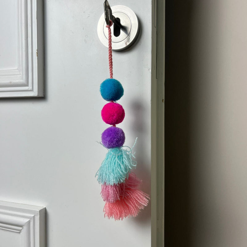 Handmade pom pom tassel hanging decor with colorful pom poms and layered pastel yarn tassels on white door background