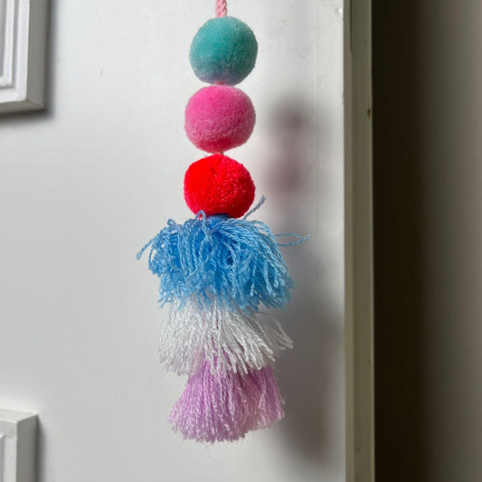 Handmade pom pom tassel hanging decor with colorful pom poms and layered yarn tassels on white door background