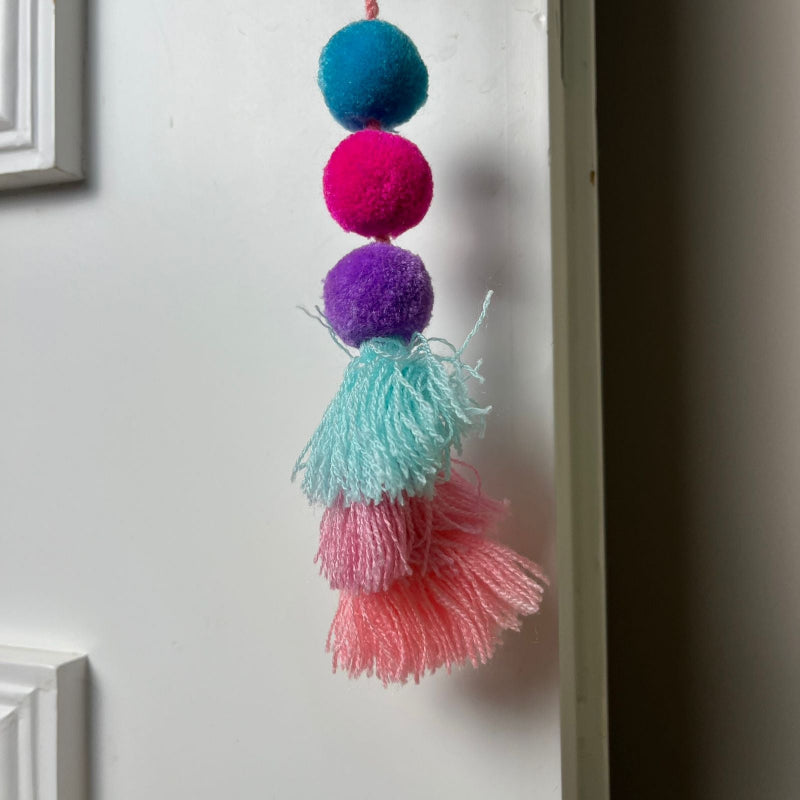 Handmade pom pom tassel hanging decor with colorful pom poms and layered pastel yarn tassels on white door background
