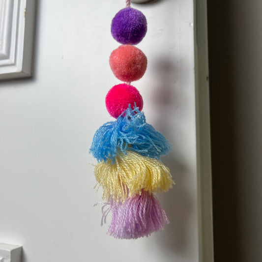 Handmade colorful pom pom tassel hanging decor with vibrant pom poms and layered yarn tassels on white door background