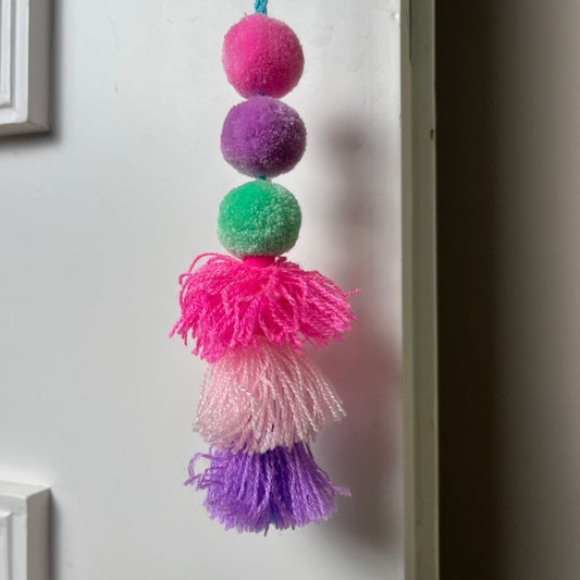 Handmade colorful pom pom tassel hanging decor with bright pom poms and layered yarn tassels on white door background