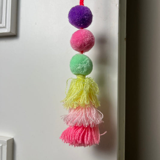 Handmade pom pom tassel hanging decor with colorful pom poms and layered yarn tassels on white door background