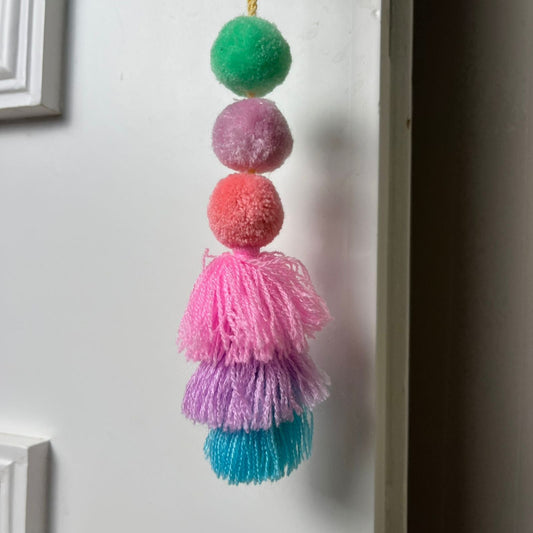 Handmade pastel pom pom tassel hanging decor with soft layered yarn tassels and fluffy pom poms on white door background