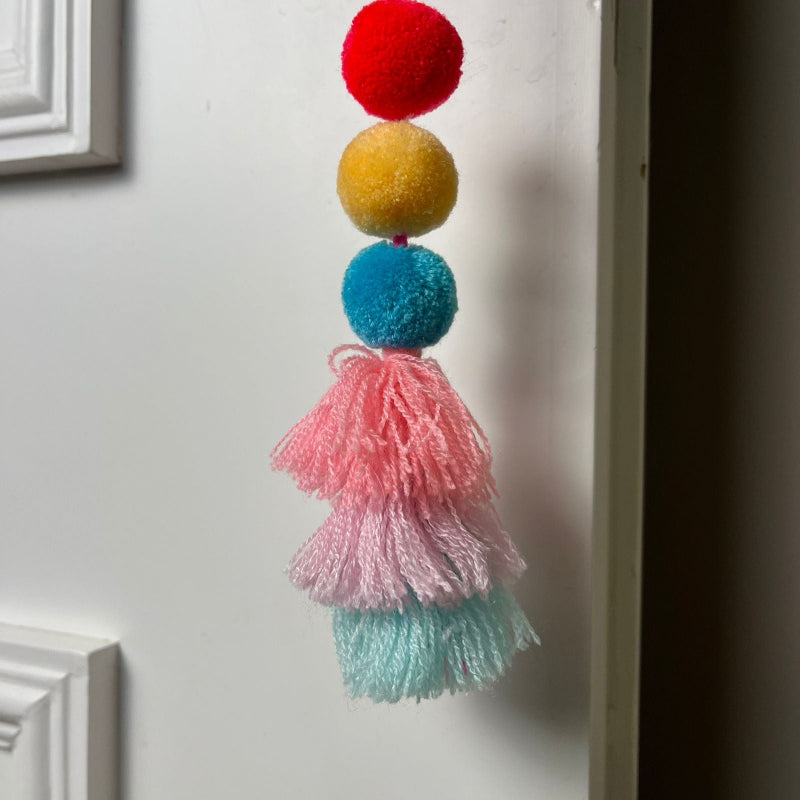 Handmade pom pom tassel hanging decor with colorful pom poms and layered pastel yarn tassels on white door background