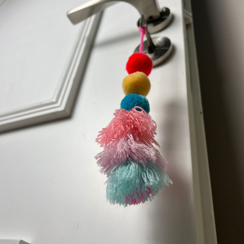Handmade pom pom tassel hanging decor with colorful pom poms and layered pastel yarn tassels on white door background
