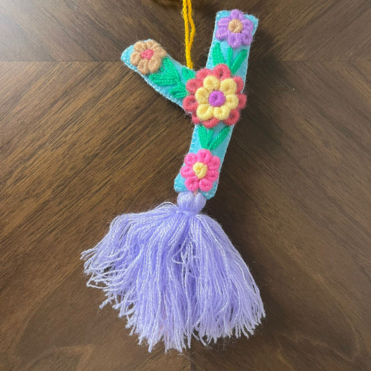 Handmade embroidered letter Y ornament with colorful floral embroidery and lavender tassel on wooden background