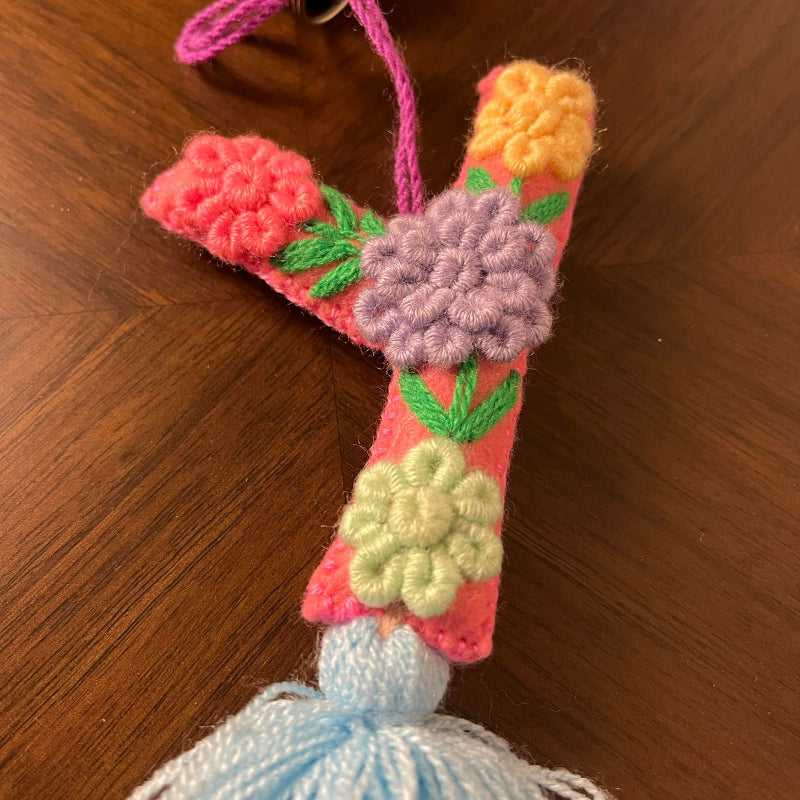 Handmade embroidered letter Y ornament with colorful floral stitching and blue tassel on wooden background
