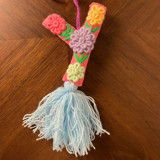 Handmade embroidered letter Y ornament with colorful floral stitching and blue tassel on wooden background