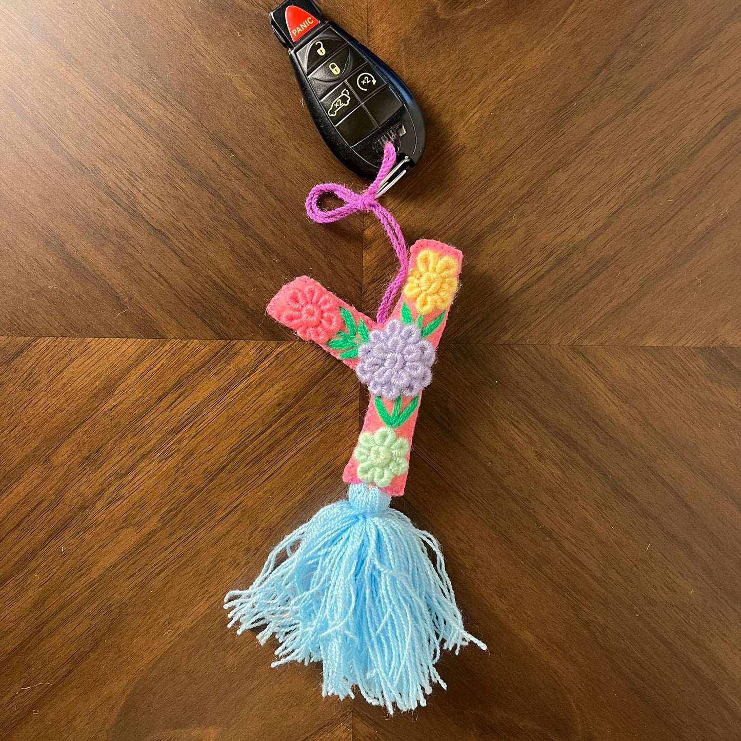 Handmade embroidered letter Y ornament with colorful floral stitching and blue tassel on wooden background