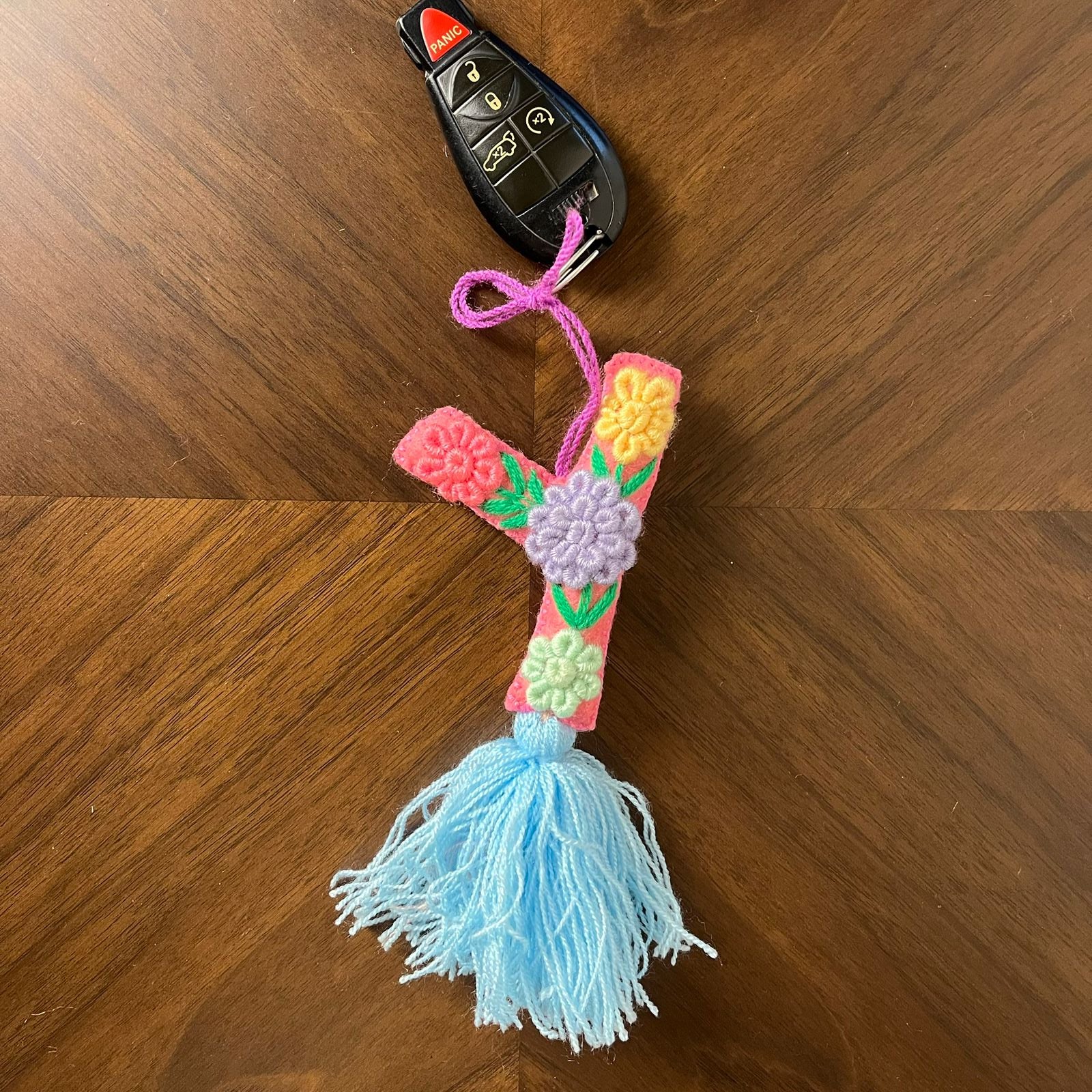 Handmade embroidered letter Y ornament with colorful floral stitching and blue tassel on wooden background