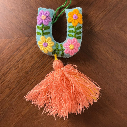 Handmade embroidered letter U ornament with colorful floral embroidery and peach tassel on wooden background