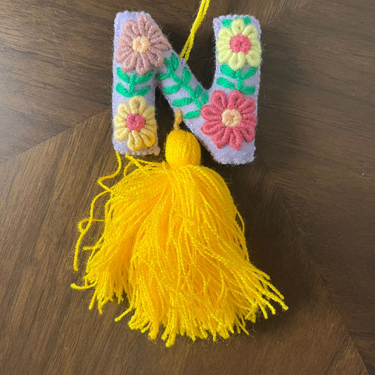 Handmade embroidered letter N ornament with colorful floral patterns and yellow tassel on wooden background