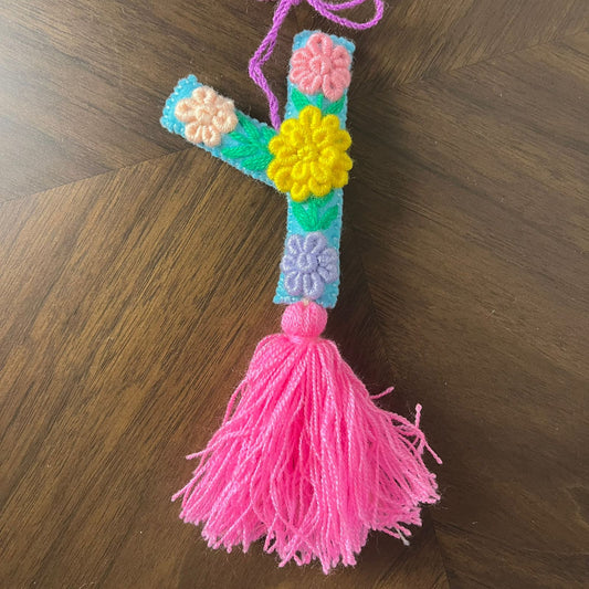 Handmade embroidered letter Y ornament with colorful floral stitching and bright pink tassel on wooden surface