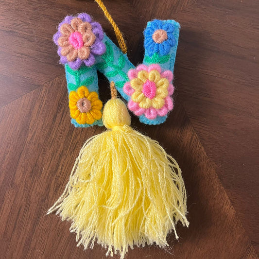 Handmade embroidered letter N ornament with colorful floral embroidery and yellow tassel on wooden background