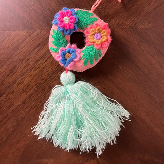 Handmade embroidered letter O ornament with colorful floral embroidery and mint green tassel on wooden background