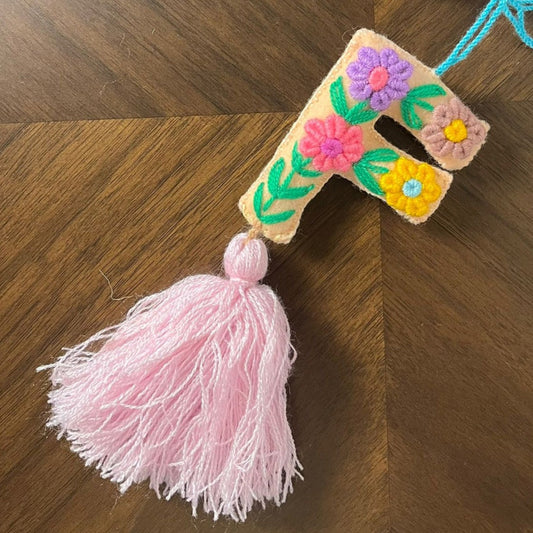 Handmade embroidered letter F ornament with colorful floral patterns and soft pink tassel on wooden background