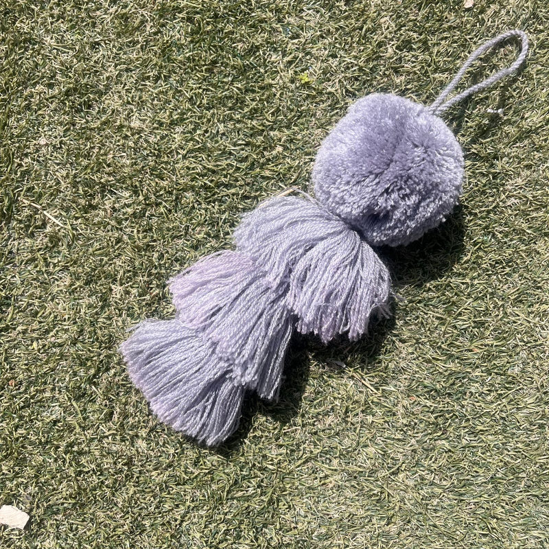 Grey fluffy tassel keychain with soft pom pom placed on grass background