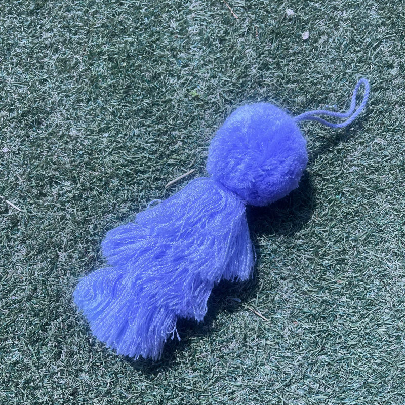 Purple fluffy tassel keychain with soft pom pom placed on grass background