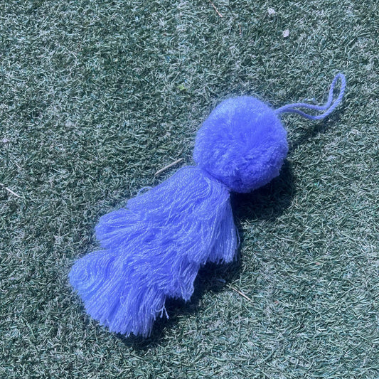 Purple fluffy tassel keychain with soft pom pom placed on grass background