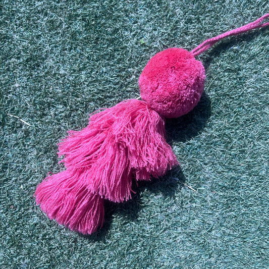 Pinky fluffy tassel keychain with soft pom pom placed on grass background