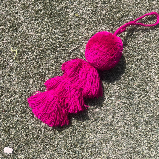 Fuchsia fluffy tassel keychain with soft pom pom placed on grass background