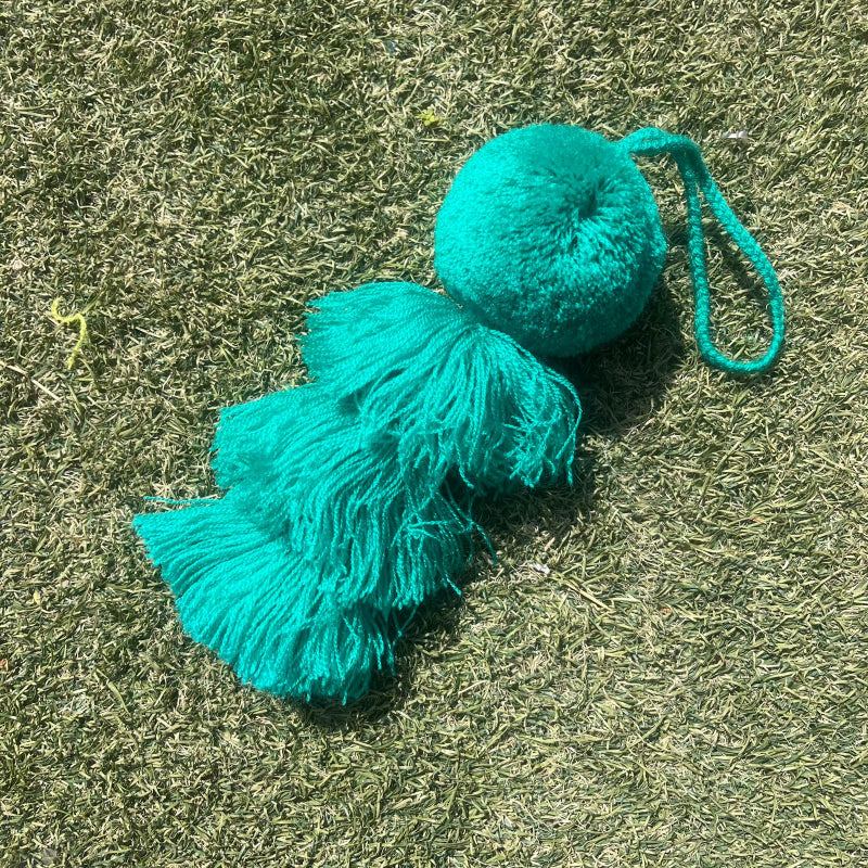 Green fluffy tassel keychain with soft pom pom placed on grass background