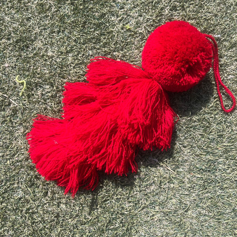 Red fluffy tassel keychain with soft pom pom placed on grass background