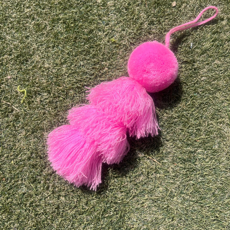 Pink fluffy tassel keychain with soft pom pom placed on grass background