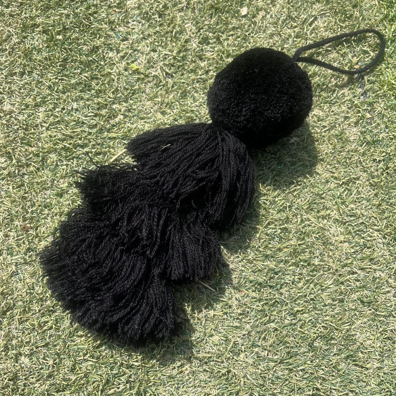Black fluffy tassel keychain with soft pom pom placed on grass background