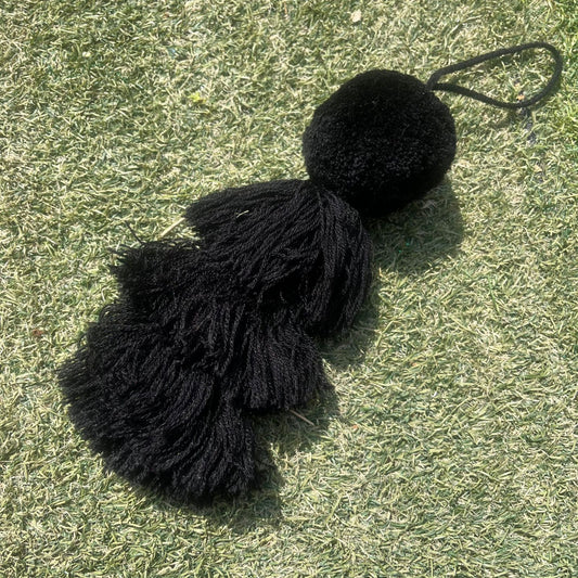 Black fluffy tassel keychain with soft pom pom placed on grass background