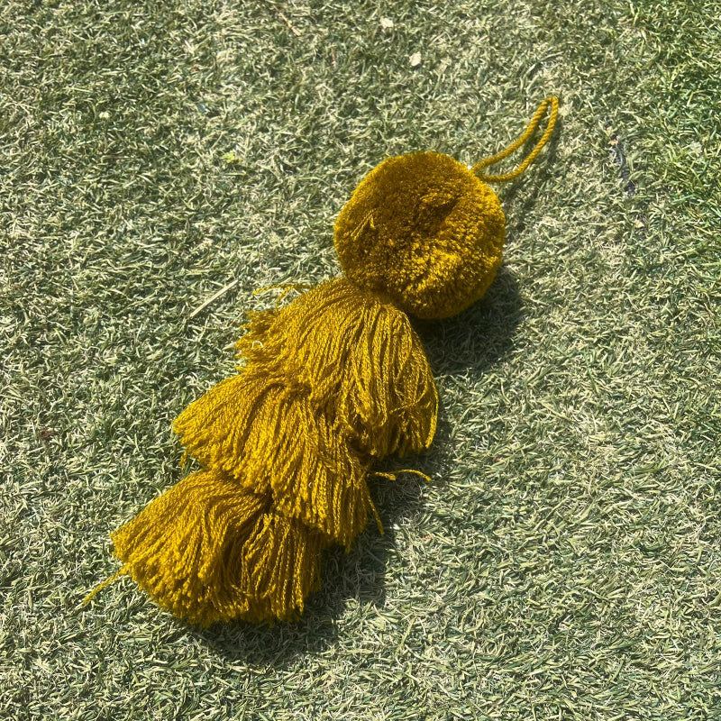 Mustard yellow fluffy tassel keychain with soft pom pom placed on grass background