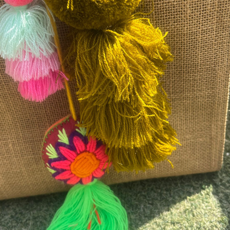 Mustard yellow fluffy tassel keychain with soft pom pom placed on grass background