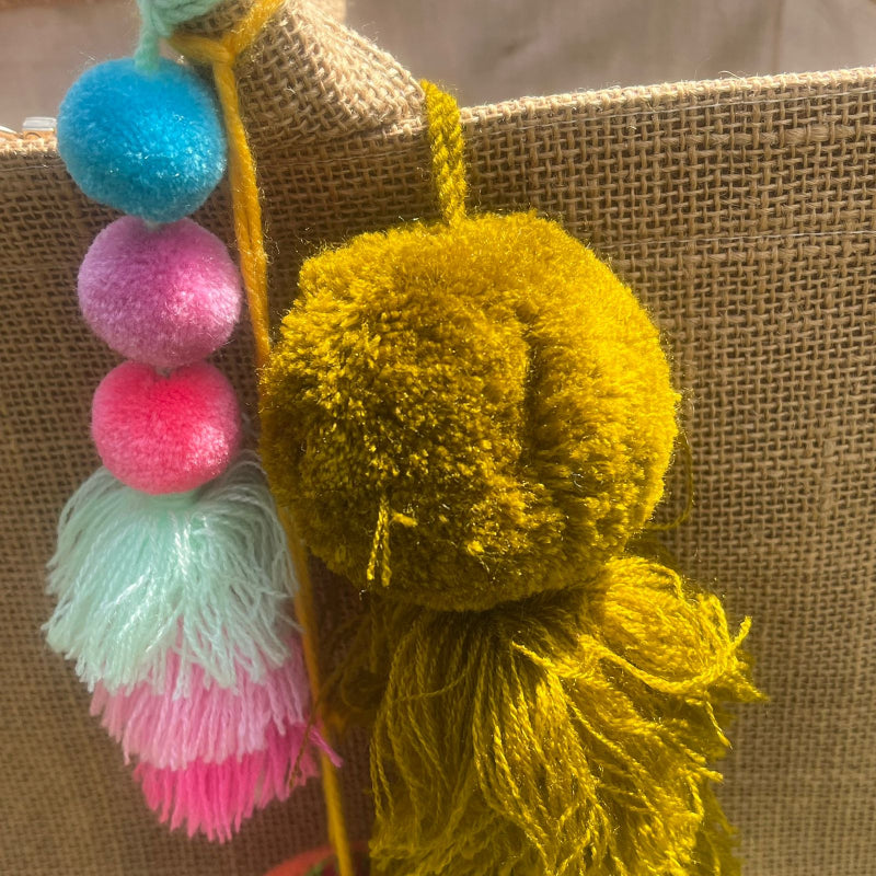 Mustard yellow fluffy tassel keychain with soft pom pom placed on grass background